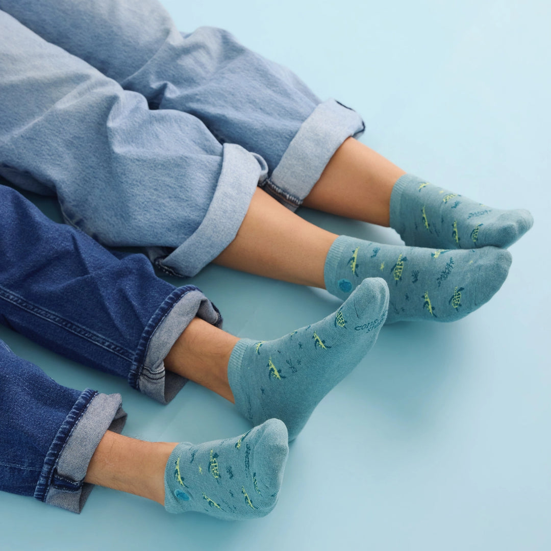 Two pairs of feet wearing blue socks with sea turtle patterns on a light blue background.