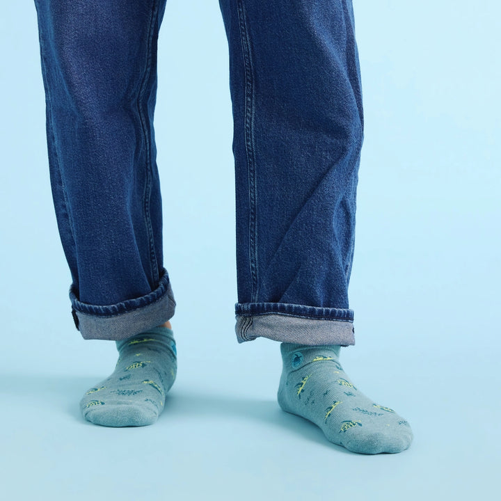 Person wearing blue jeans and light blue socks with sea turtle accents on a light blue background
