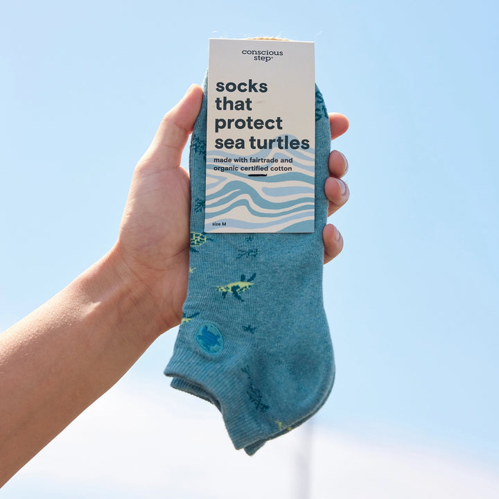Hand holding a pair of blue socks with a 'conscious step' label against a clear blue sky.