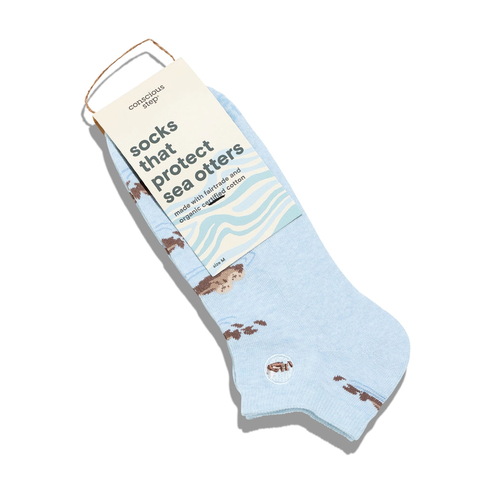 Light blue socks with brown sea otter illustrations on a white background, featuring a packaging label.