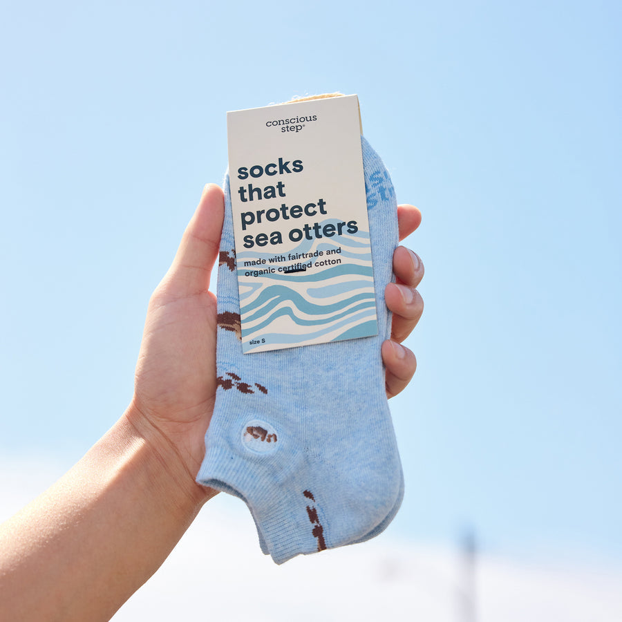 Hand holding a pair of socks with a packaging label against a clear blue sky