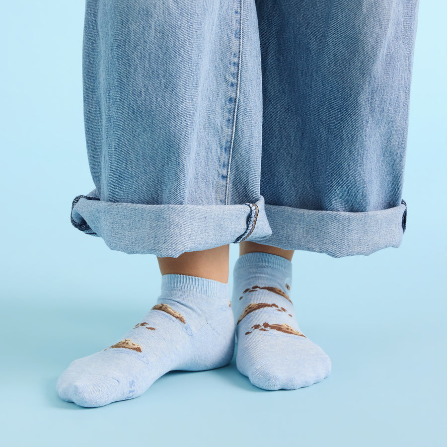 Light blue socks with sea otters worn with rolled-up jeans on a light blue background