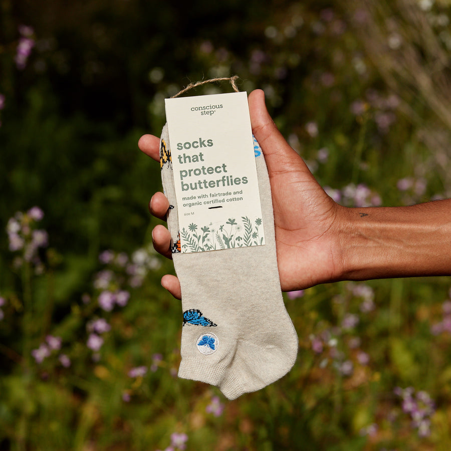 Hand holding a pair of socks with a label that reads 'socks that protect butterflies' against a natural background.