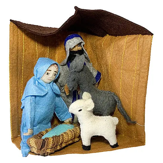 Felted nativity scene with a brown stable backdrop, a kneeling figure in light blue robes beside a manger, a standing figure in gray and blue robes behind, and a small white lamb in front, photographed on a white background.
