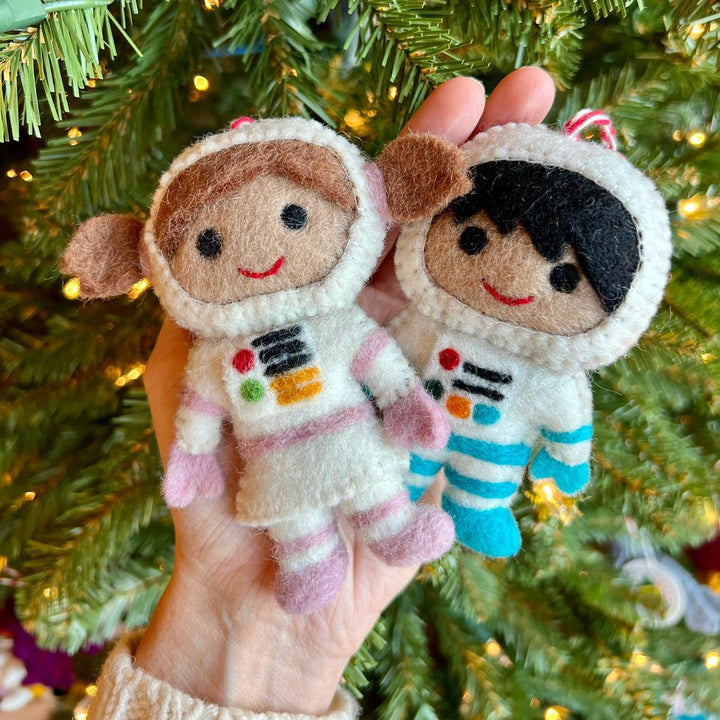 Two felt astronaut ornaments held against a Christmas tree background