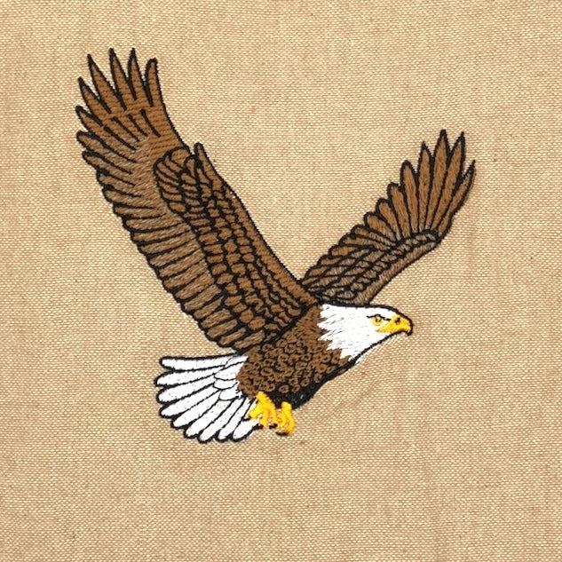 Embroidered bald eagle design on a beige fabric background, showing brown wings, white head and tail, and yellow beak and talons.