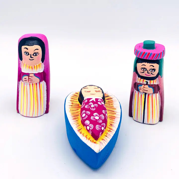 Three hand-painted wooden pieces on a white background, featuring a mary and Joseph doll standing on either side of a baby Jesus lying in a blue cradle.