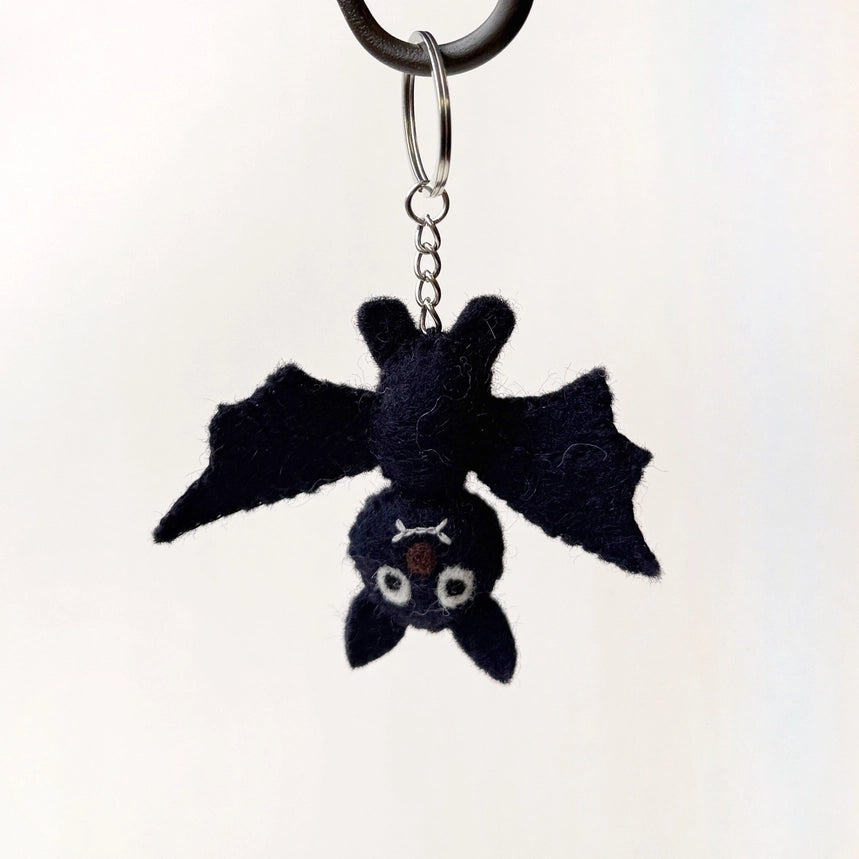 A small felt bat keychain charm with outstretched wings, hanging from a silver metal ring and chain against a plain light background.