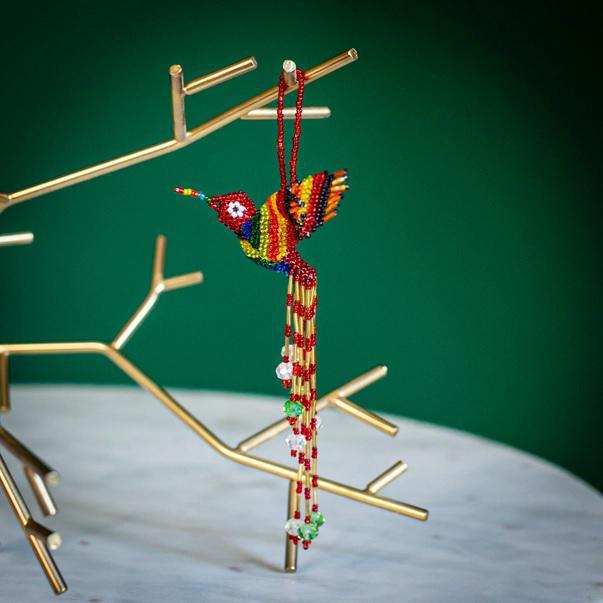 A colorful beaded hummingbird ornament hanging from a loop, with a design that includes multiple beads in mainly red and yellow colors.