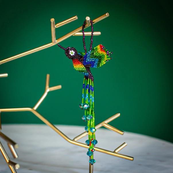 A colorful beaded hummingbird ornament hanging from a loop, with a design that includes multiple beads in blue and green colors.