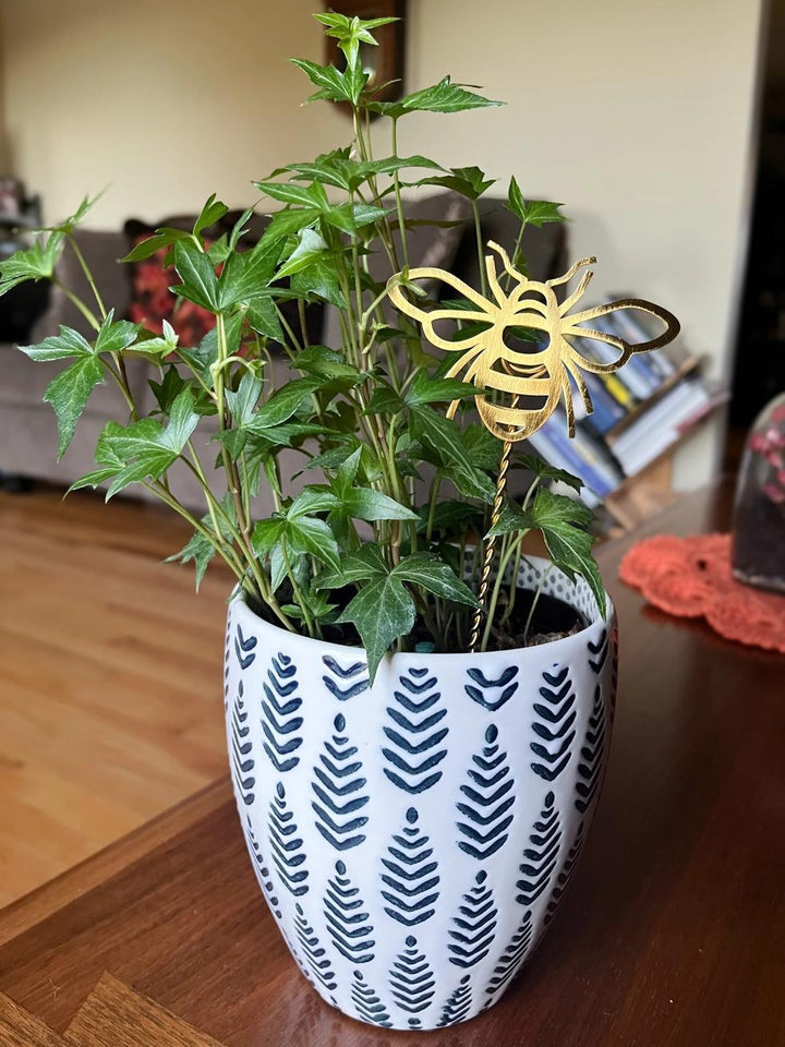 Potted plant with a decorative bee plant stake on a wooden surface