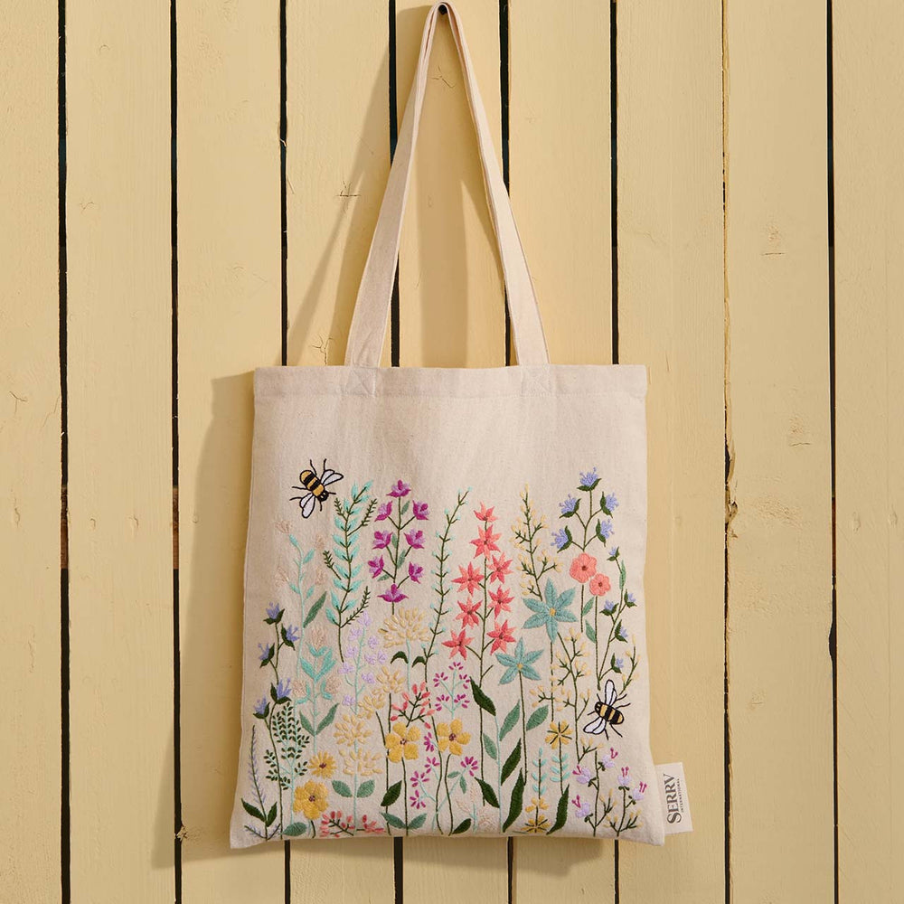 Tote bag with floral design and bee illustrations hanging on a wooden wall