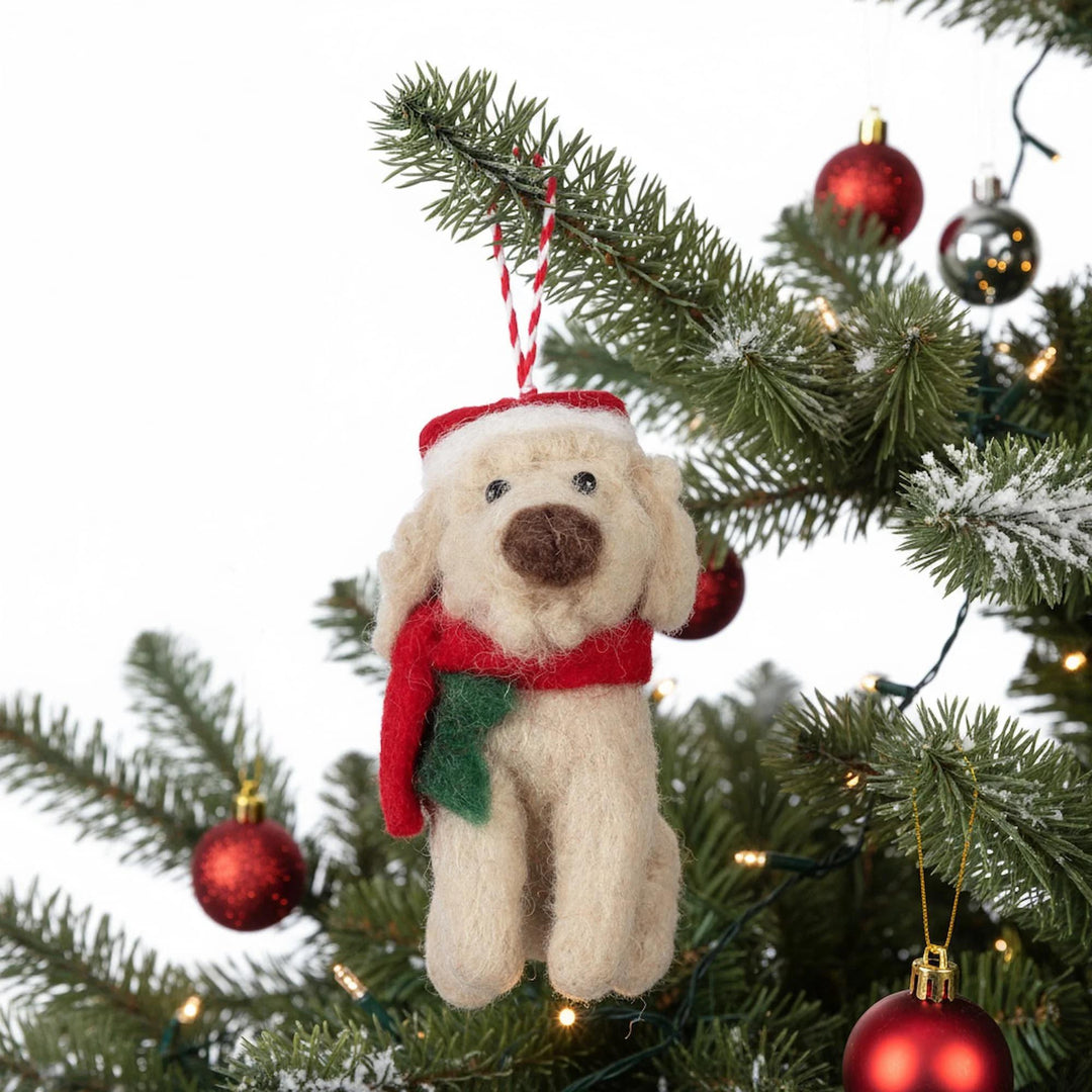 Dog-shaped Christmas ornament with a red scarf hanging on a decorated tree.