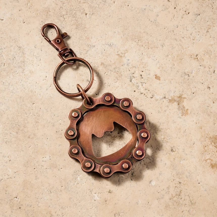 Copper keychain with a unique bike chain design on a beige background