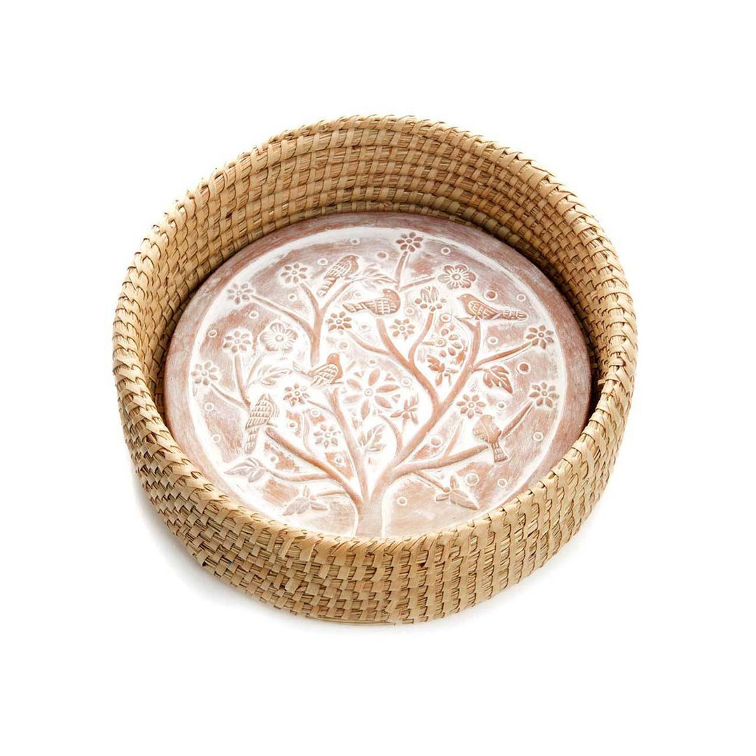 Decorative stone with tree and bird design inside a woven basket on a white background