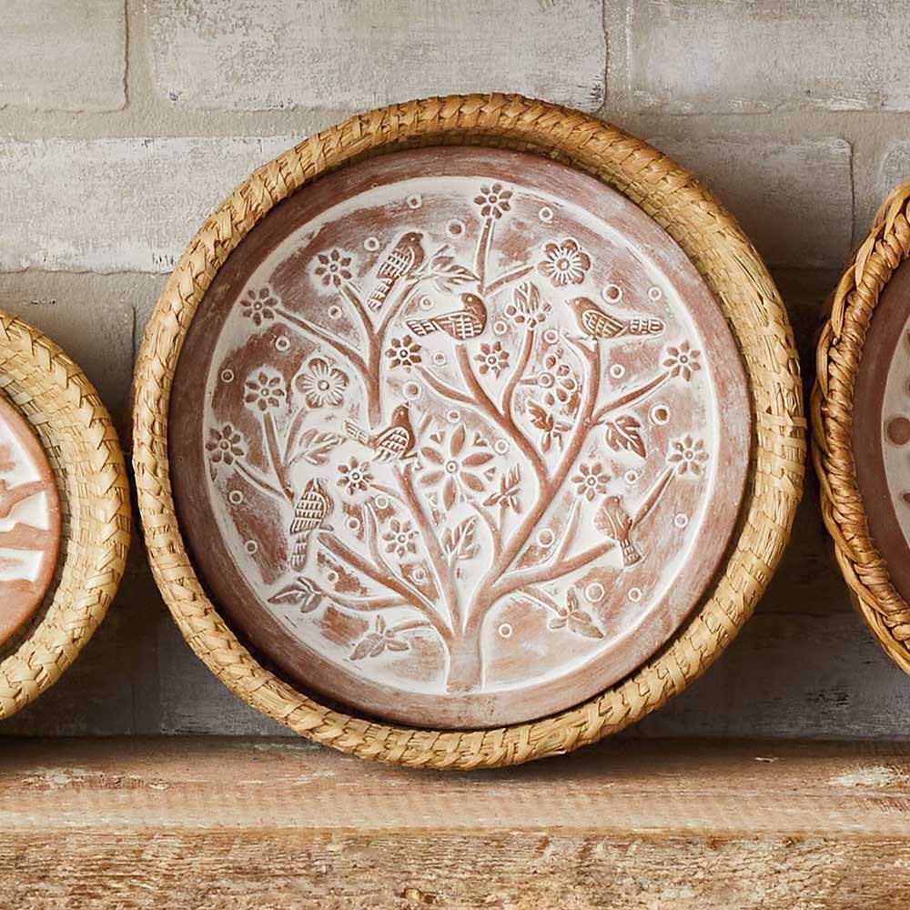 Decorative terracotta breadwarmer with embossed designs on a wooden surface.
