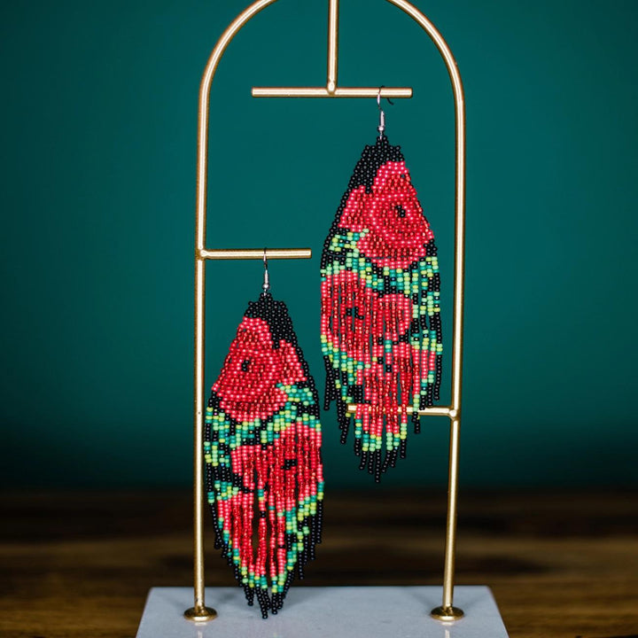 Beaded rose fringe earrings on a gold stand against a teal background