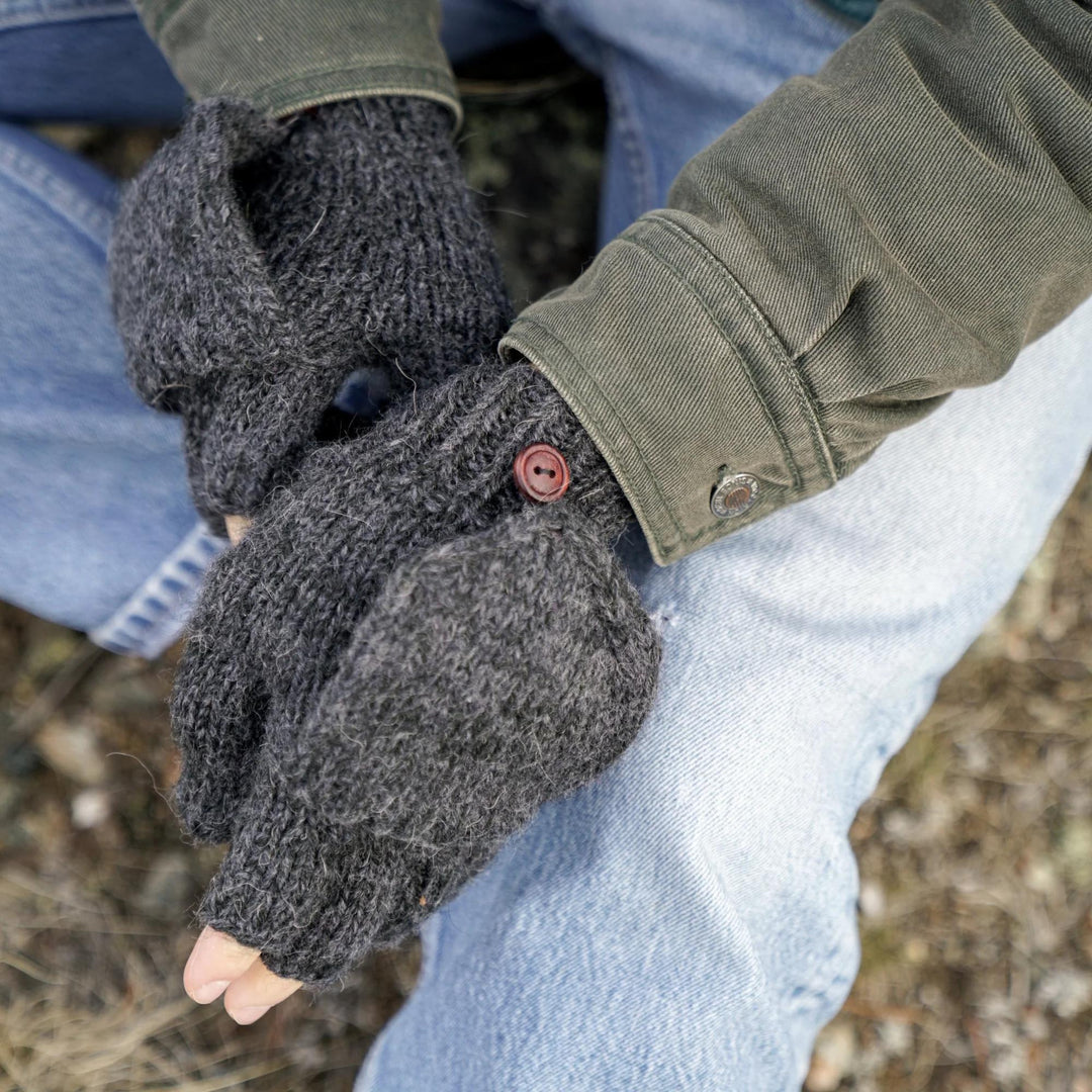 Person wearing dark gray fingerless gloves with a button, sitting outdoors.