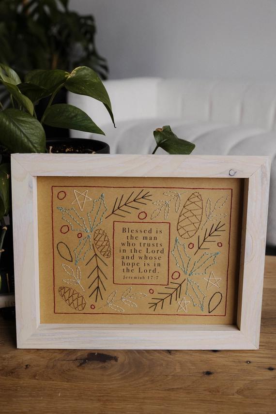 Framed embroidered artwork with decorative elements on a wooden surface.
