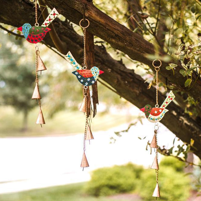 Three hand-painted bird wind chimes with tiered cone bells, made from upcycled metal, hanging from a tree.