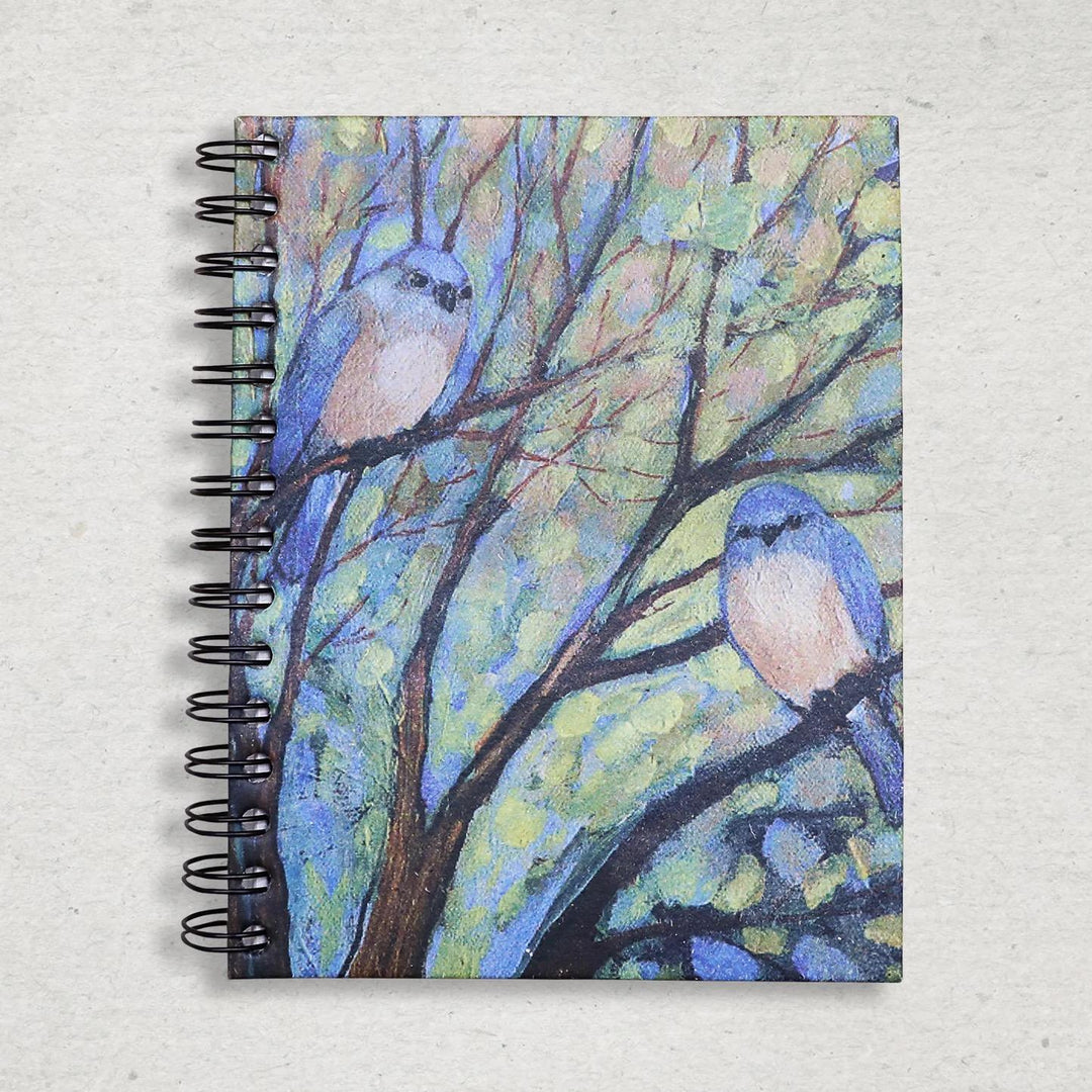 Elephant poo notebook with a cover featuring two blue birds on branches against a leafy green background.