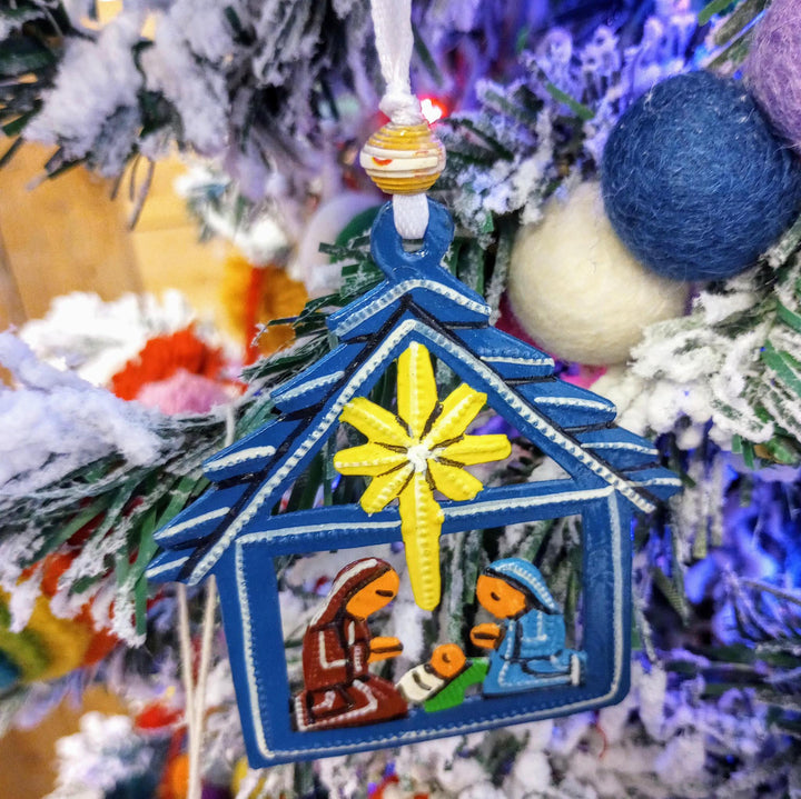 a blue metal nativity ornament with a Christmas tree background