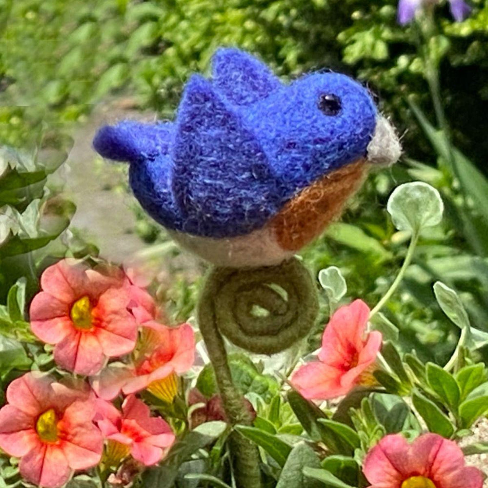 Blue felted bird among pink flowers and green foliage