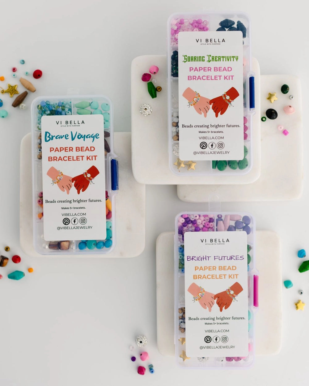 Three clear plastic bead kits with white labels are arranged on a white background. The kits contain colorful paper bead bracelets, and small loose beads are scattered around them.