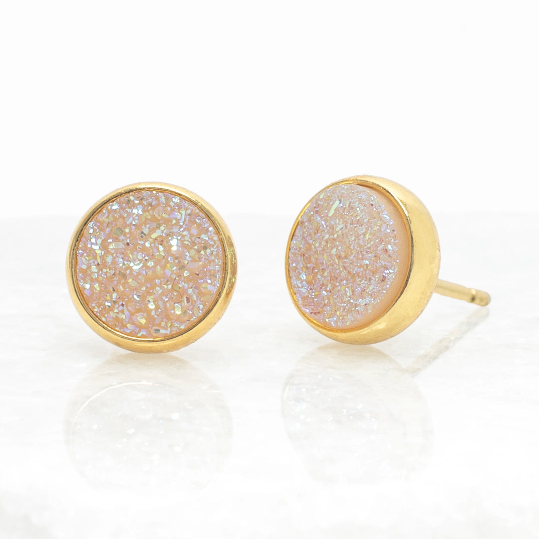 Gold-framed earrings with a light-colored, textured center on a white background