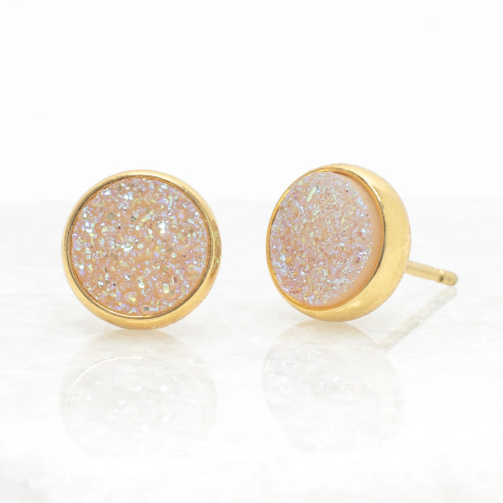 Gold-framed earrings with a light-colored, textured center on a white background