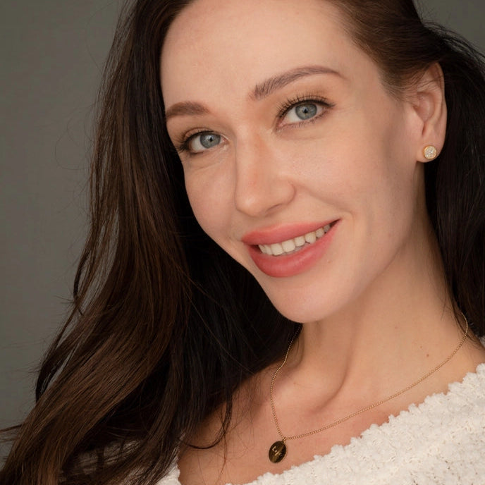 Woman with long brown hair wearing a white textured top against a gray background
