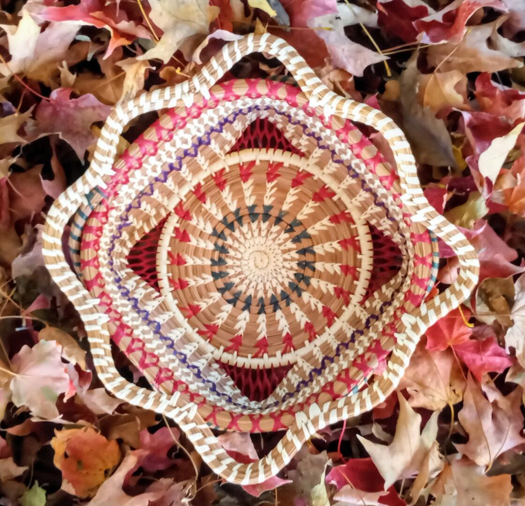 Decorative woven basket with a colorful pattern on a bed of autumn leaves.