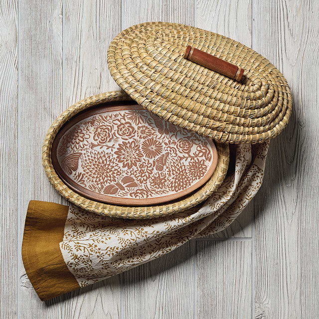 Woven basket with floral-patterned lid and wooden handle on a light wooden surface