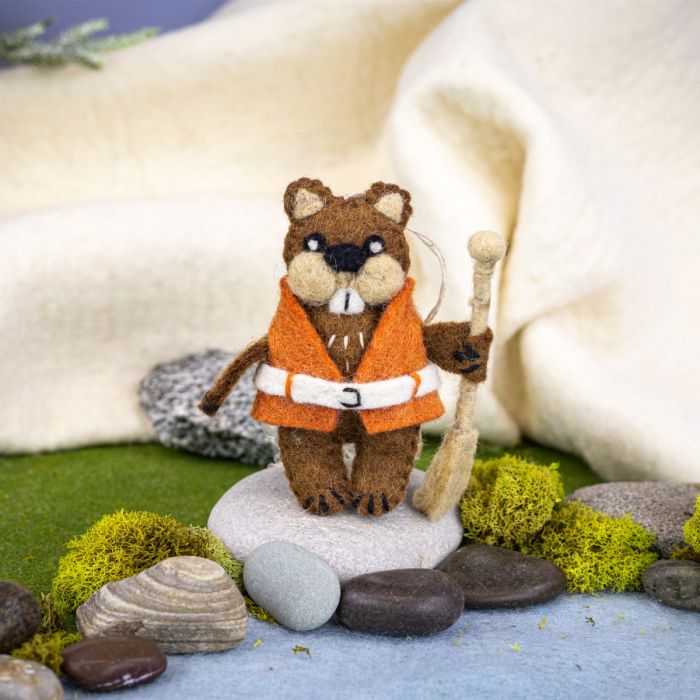Felt beaver ornament in an orange jacket with a fishing rod on a miniature landscape.