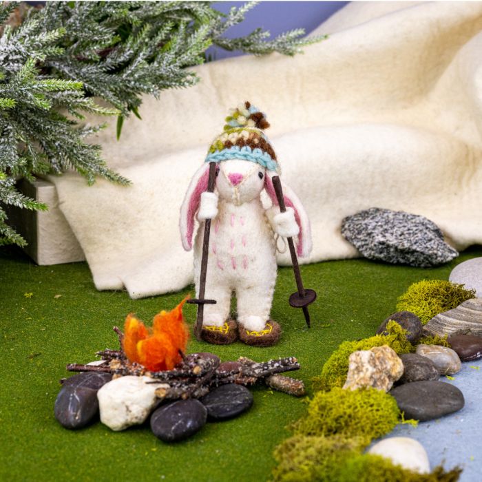 Stuffed bunny with skis and a hat ornament  by a campfire in a miniature landscape