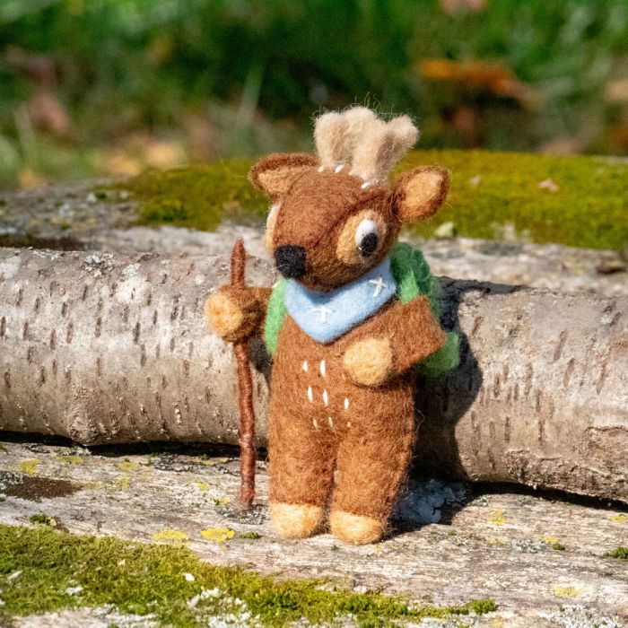 Stuffed deer ornament with a walking stick on a log with a natural background