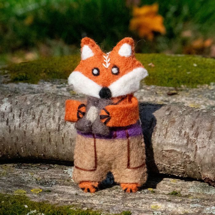 Felt fox ornament holding binoculars on a log with a natural background