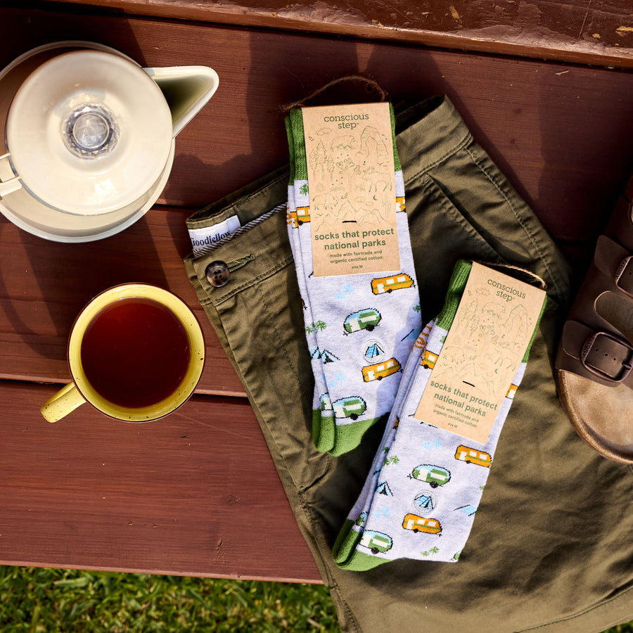 Two pairs of socks with camping design on a wooden surface with a cup of tea and pants