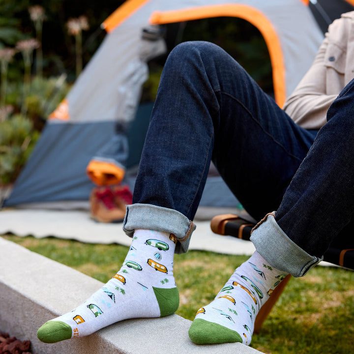 Person sitting outdoors with colorful socks featuring camping designs, camping tent in the background.