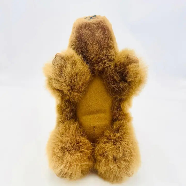 A brown alpaca fur capybara toy shown from the back, featuring a solid brown padded center and small embroidered details on the top of its head, set against a plain white background.