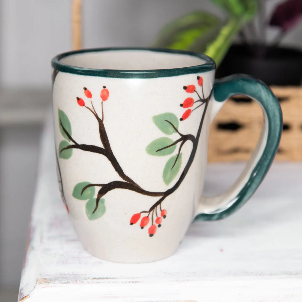 Ceramic mug with a branch and berry design on a white surface.
