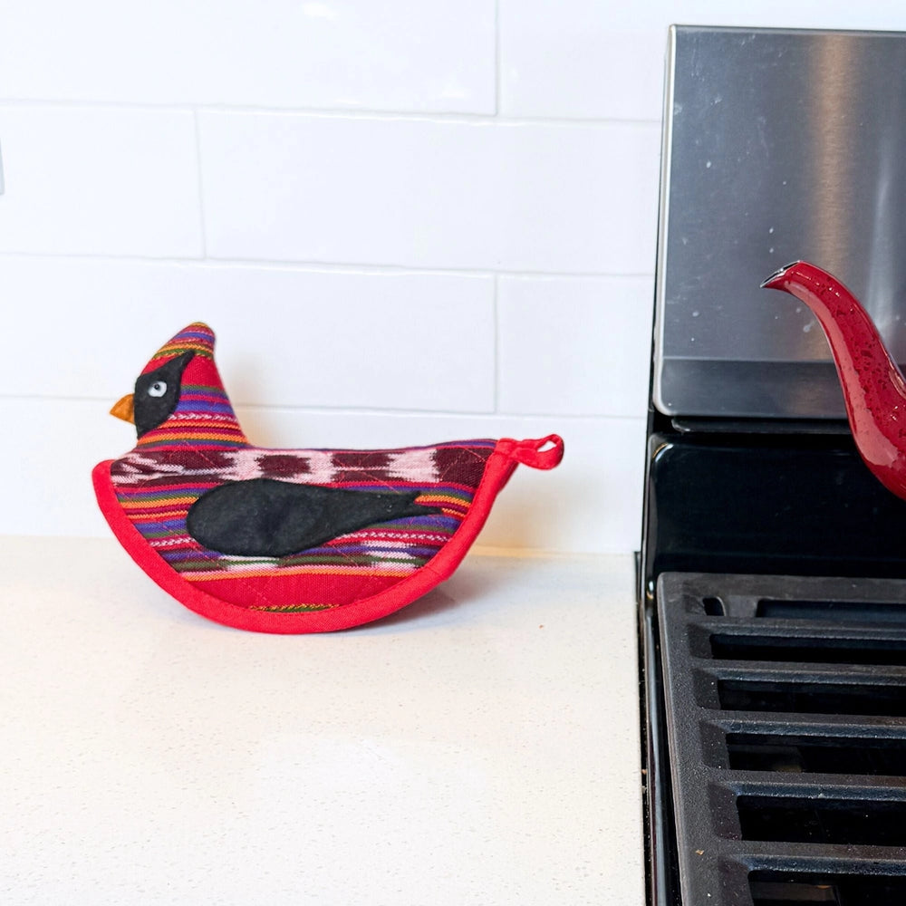 Colorful cardinal-shaped pot holder on a stove against a white tiled wall.