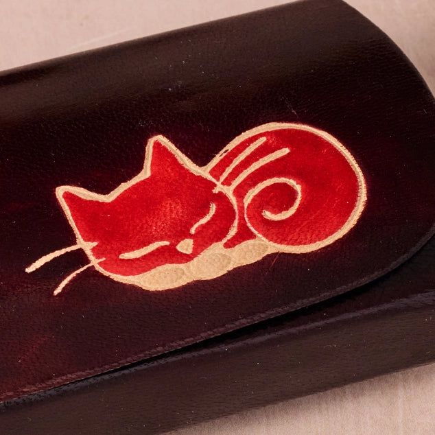 Black leather glasses case with a red and white cat illustration on a beige background
