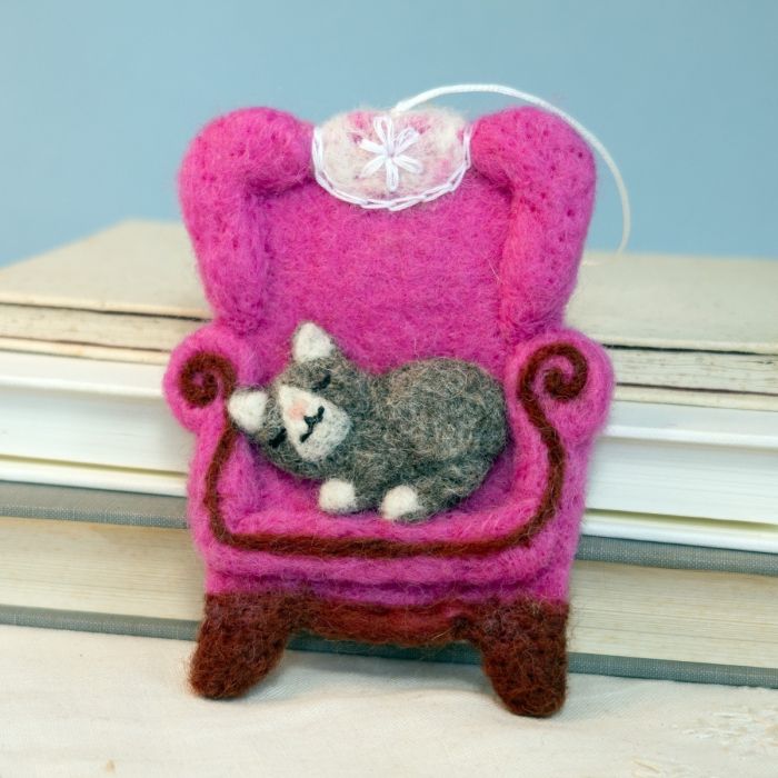 Felted toy of a cat on a pink chair with a blue background