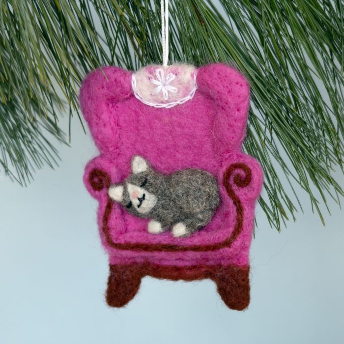 Felt ornament of a cat in a pink chair hanging on a Christmas tree.