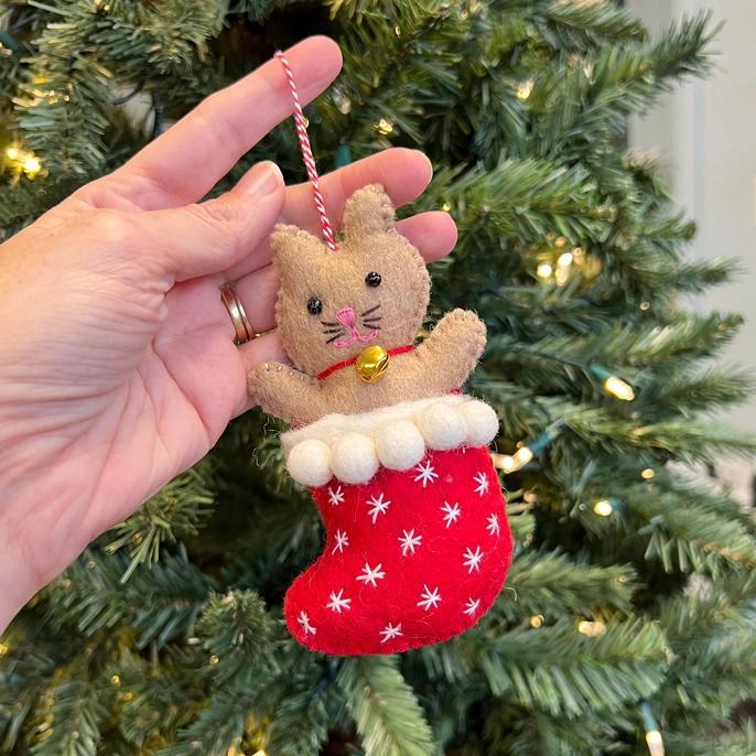 a person holding a cute felted ornament of a cat in a christmas stocking. 