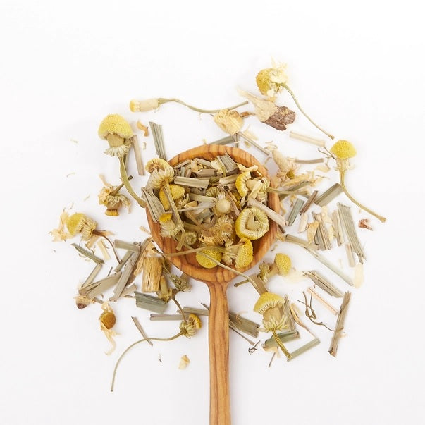 Wooden spoon filled with dried Chamomile dream tea leaves on a white background