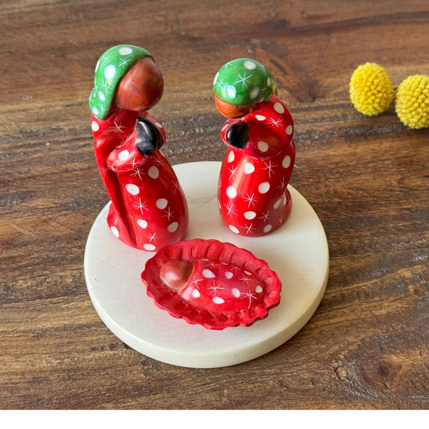 Decorative nativity figurines with red and white polka dot patterns on a wooden surface.