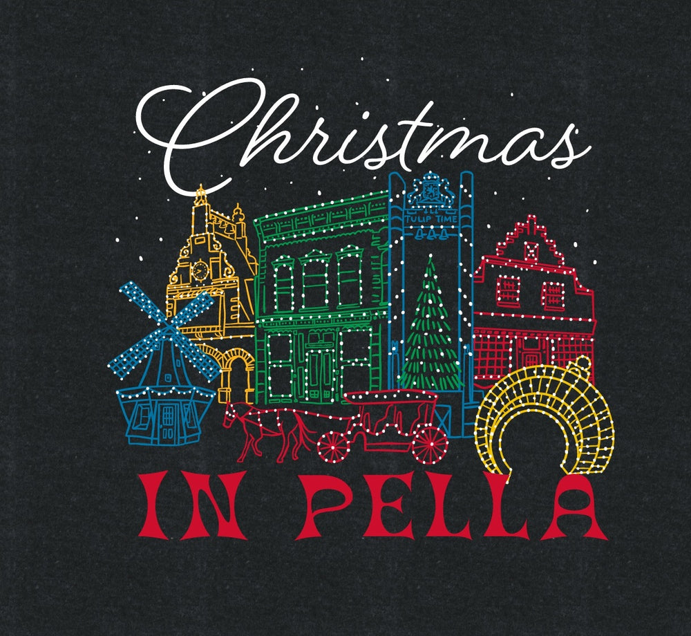A dark charcoal heather graphic print featuring colorful Christmas-themed buildings outlined with lights, a green Christmas tree, and the words 'Christmas IN PELLA' in white and red lettering.