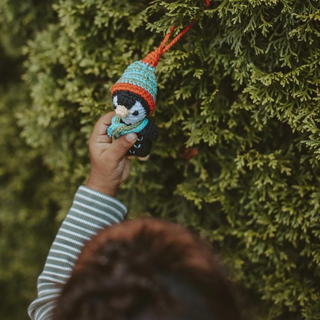 Child holding a small knitted penguin ornament against a green bush background